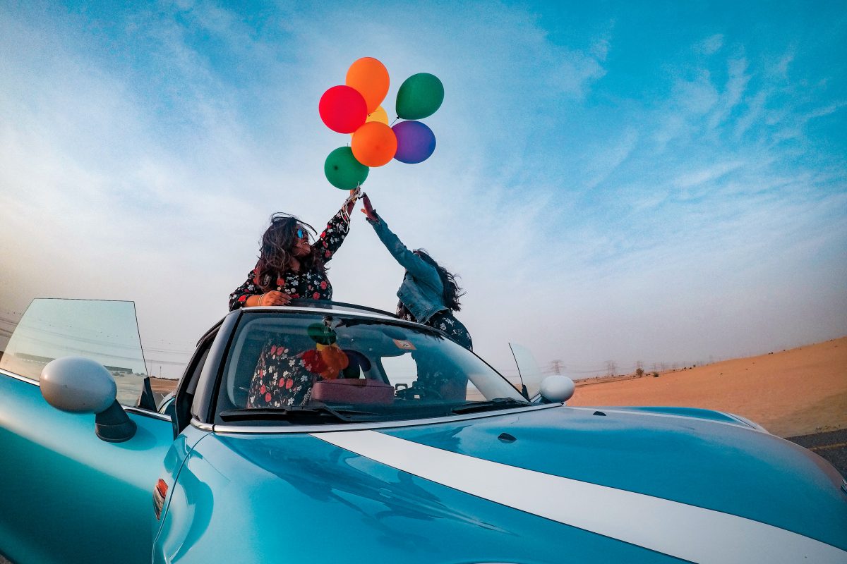 Two people holding balloons while inside a car.