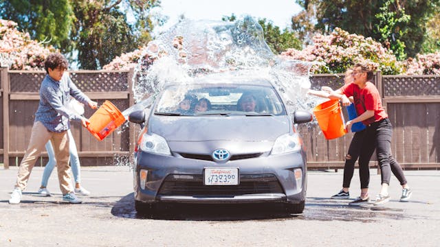 People throwing buckets of water on a car.