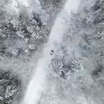 An aerial shot of a car driving through a snow covered forest.