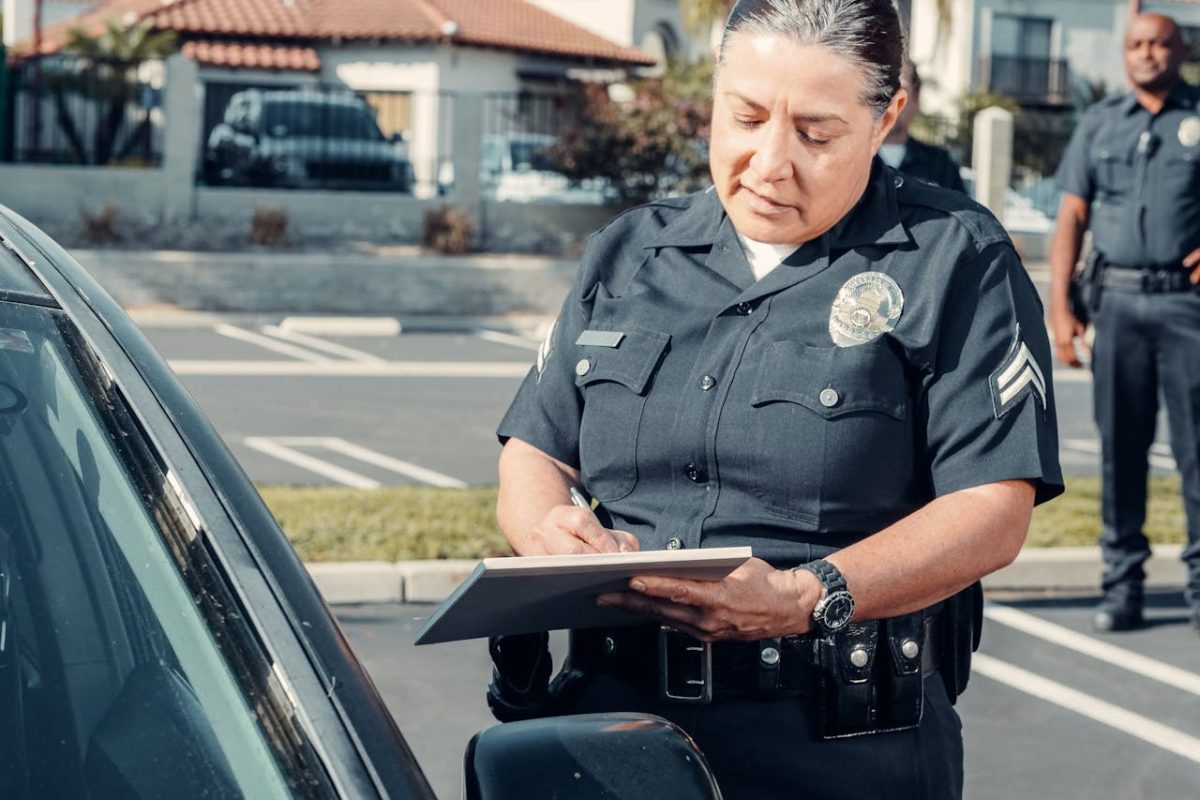 A police officer standing next to a car while writing something on a clip board.
