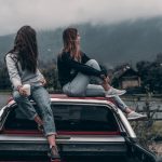 Two women sitting on top of a car.