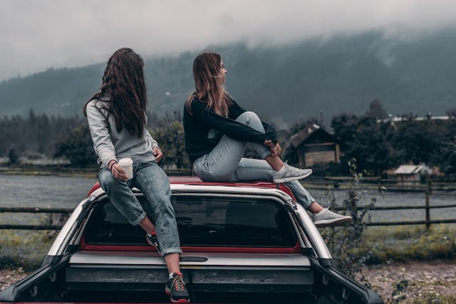Two women sitting on top of a car.
